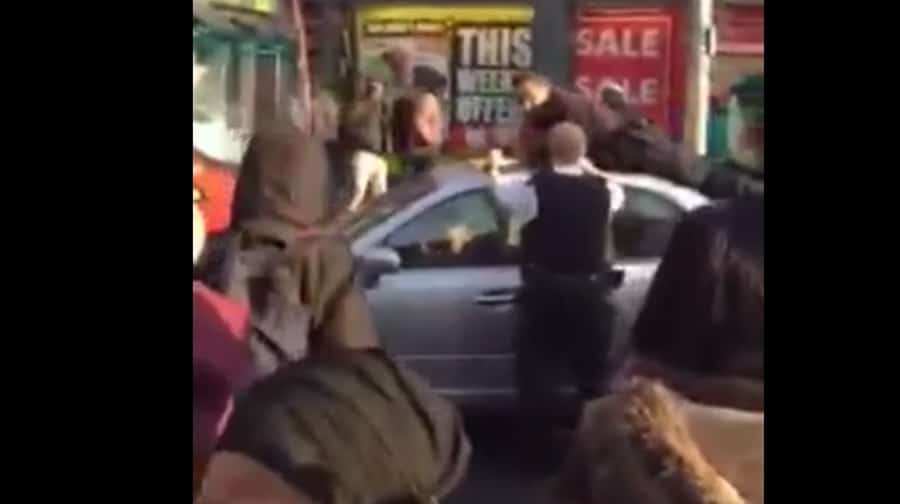 An onlooker's video shows at least five officers and a crowd of people as the naked man refuses to get out of the car