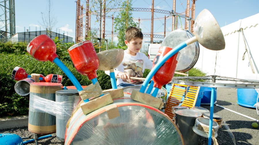 A visitor plays a drum set made out of recycled waste.
