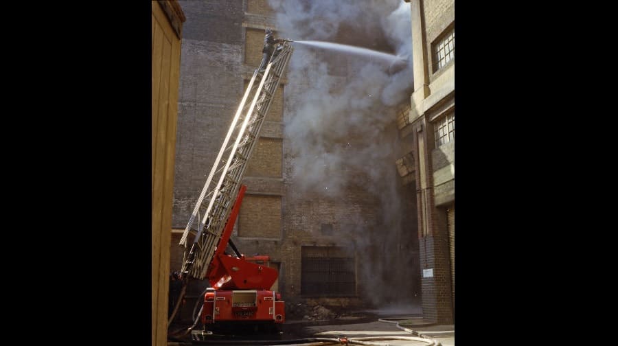A firefighter faces thick smoke while tackling the fire from the top of a turntable ladder