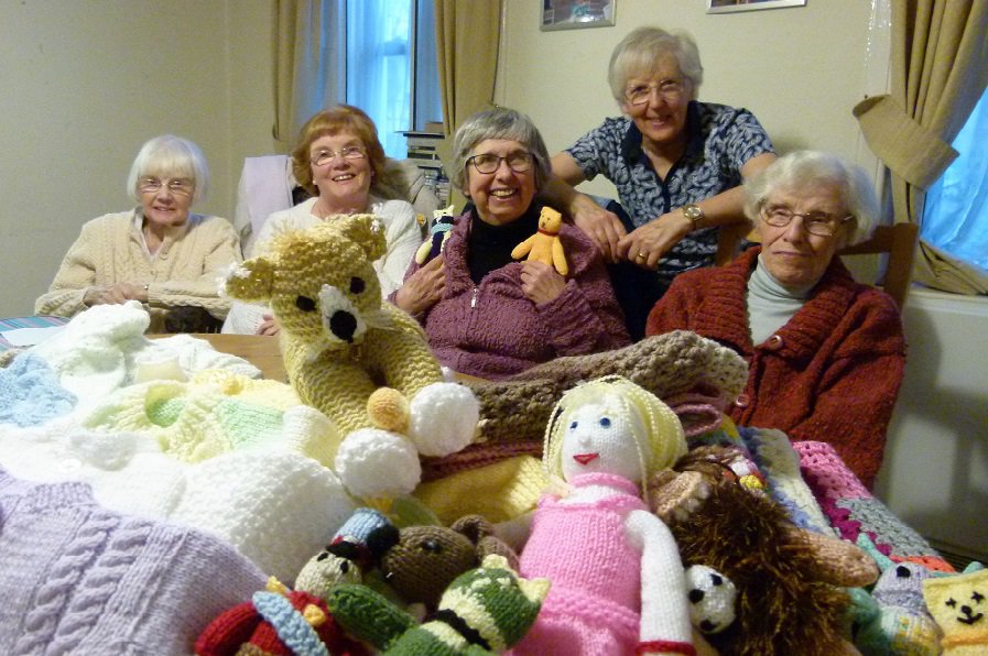L-R Knitters Peggy Ball, Jean Ball, Freda Neville, Gwen Hickman, and group founder Sheila Grantham with some of their handmade blankets, children’s clothing, and soft toys