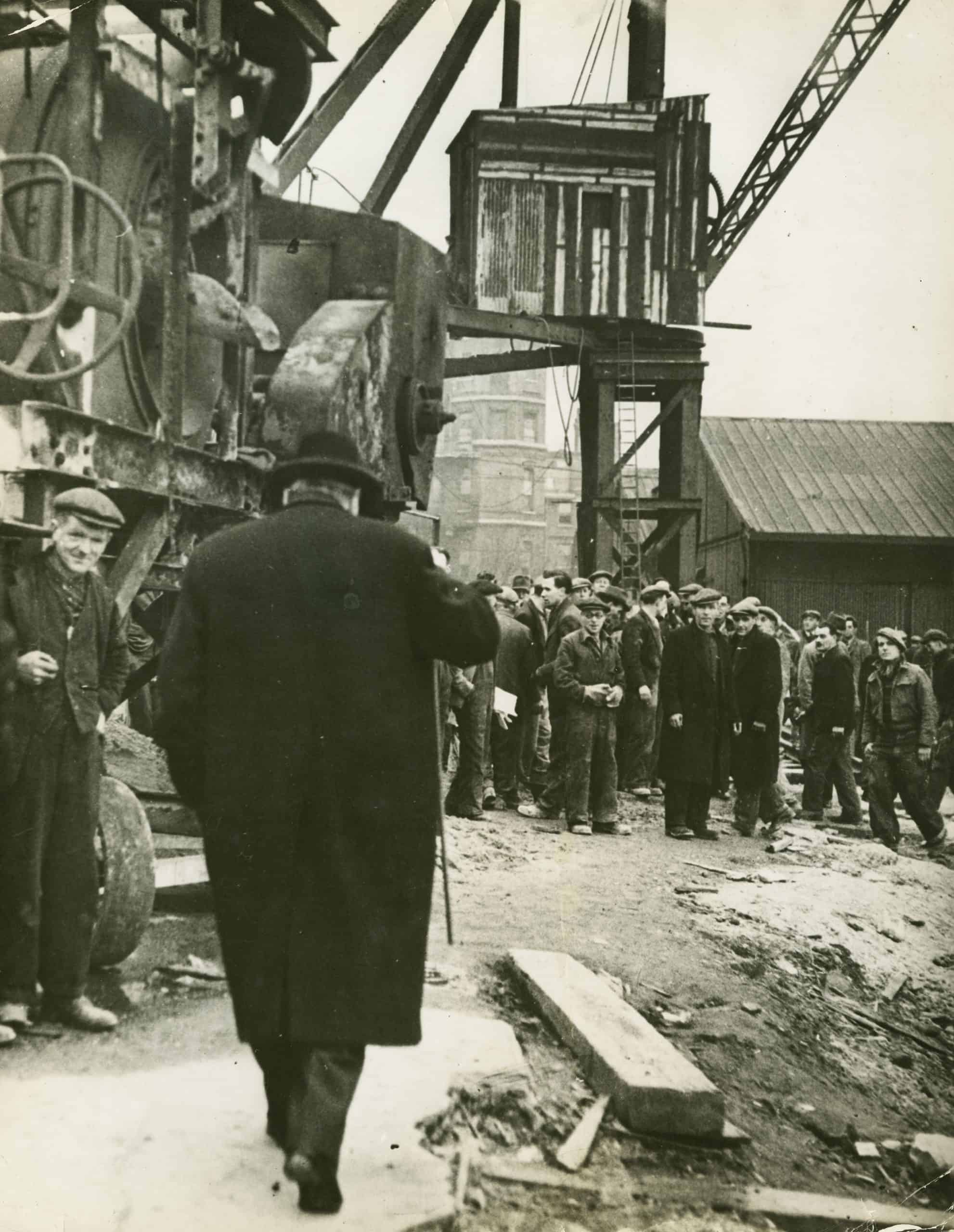 The Prime Minister, Winston Churchill, with some of the thousands of British workers engaged upon the construction of sections of the prefabricated ports, East India Dock, 1944. Two prefabricated ports, each as big as Gibralter, were manufactured in Britain in sections, towed across the channel, and set down off the coast of Normandy. The use of the prefabricated Port greatly simplified the problem of supplying the Allied Armies in France. The dock was pumped dry to allow for the building of concrete ‘harbours’ that would be towed to France for 
‘D Day’. British Official Photograph, No.P.1771.WB.Ministry of Supply.